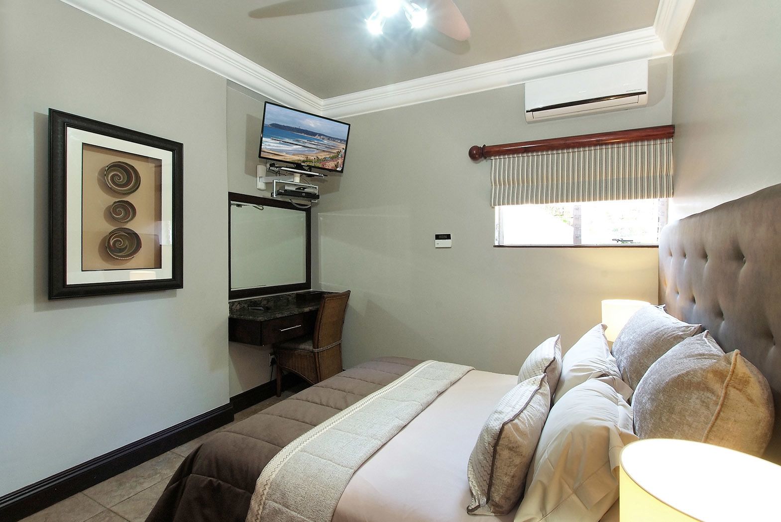 Un dormitorio con cama, escritorio, silla, televisor y ventana con cortinas.