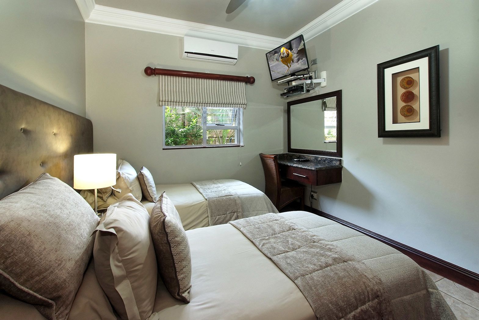 A hotel room with a large bed, a desk, a mirror, and a window with a view of greenery.