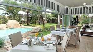 Ett utomhusområde med bord uppdukat för frukost, med utsikt över en swimmingpool och frodig grönska.