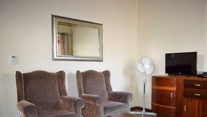A living room with two armchairs, a wooden coffee table, a television on a wooden cabinet, and a standing fan. - Paul Kruger 63 (Robertson)