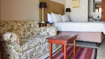 A hotel room with a floral sofa, a wooden table, a bed with white bedding, and a patterned rug.