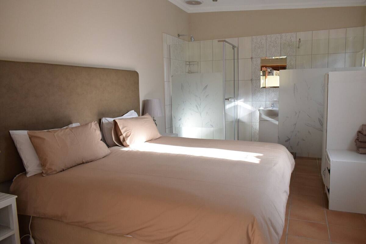 A bedroom with a large bed, a nightstand, a bedside table, a mirror, and a bathroom with a shower and sink.