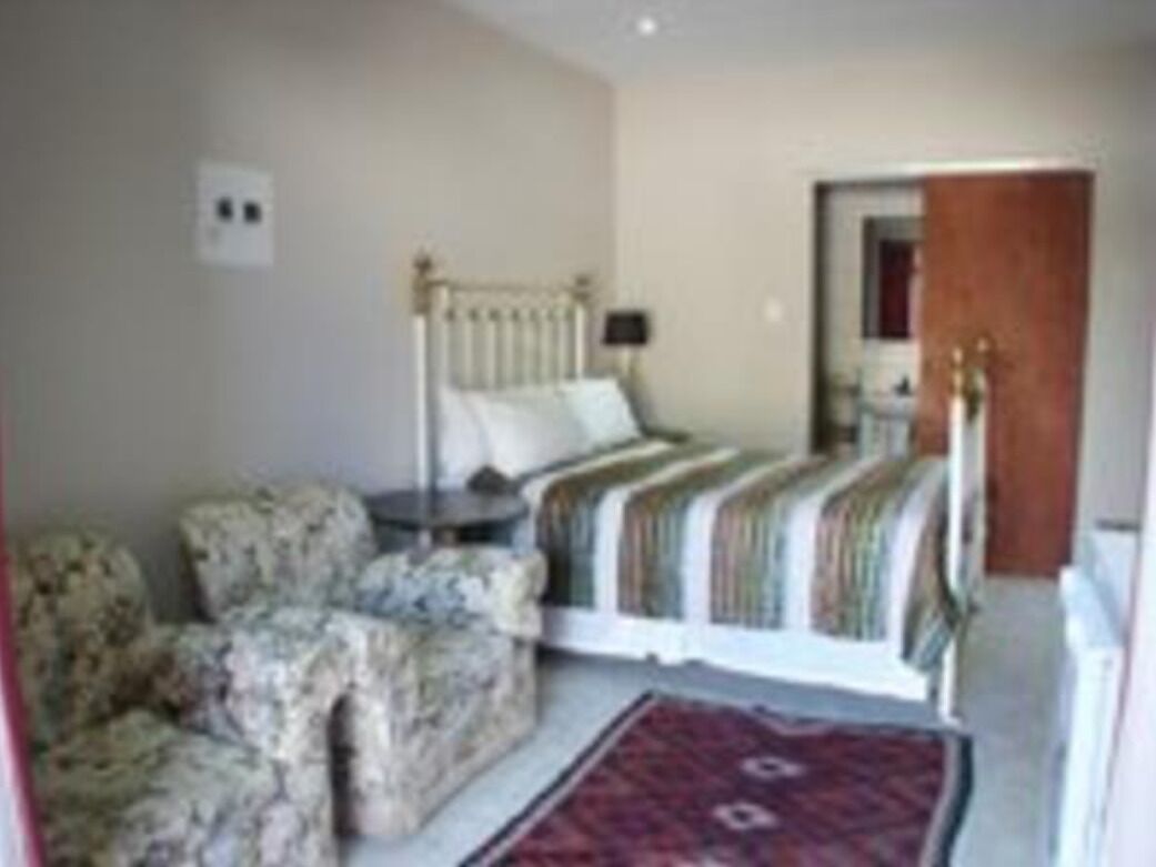 A bedroom with a bed, a nightstand, a chair, and a red rug.