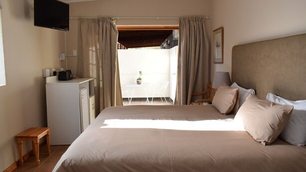 A bedroom with a bed, a desk, a television, and a view of an outdoor area. - Paul Kruger 63 (Robertson)