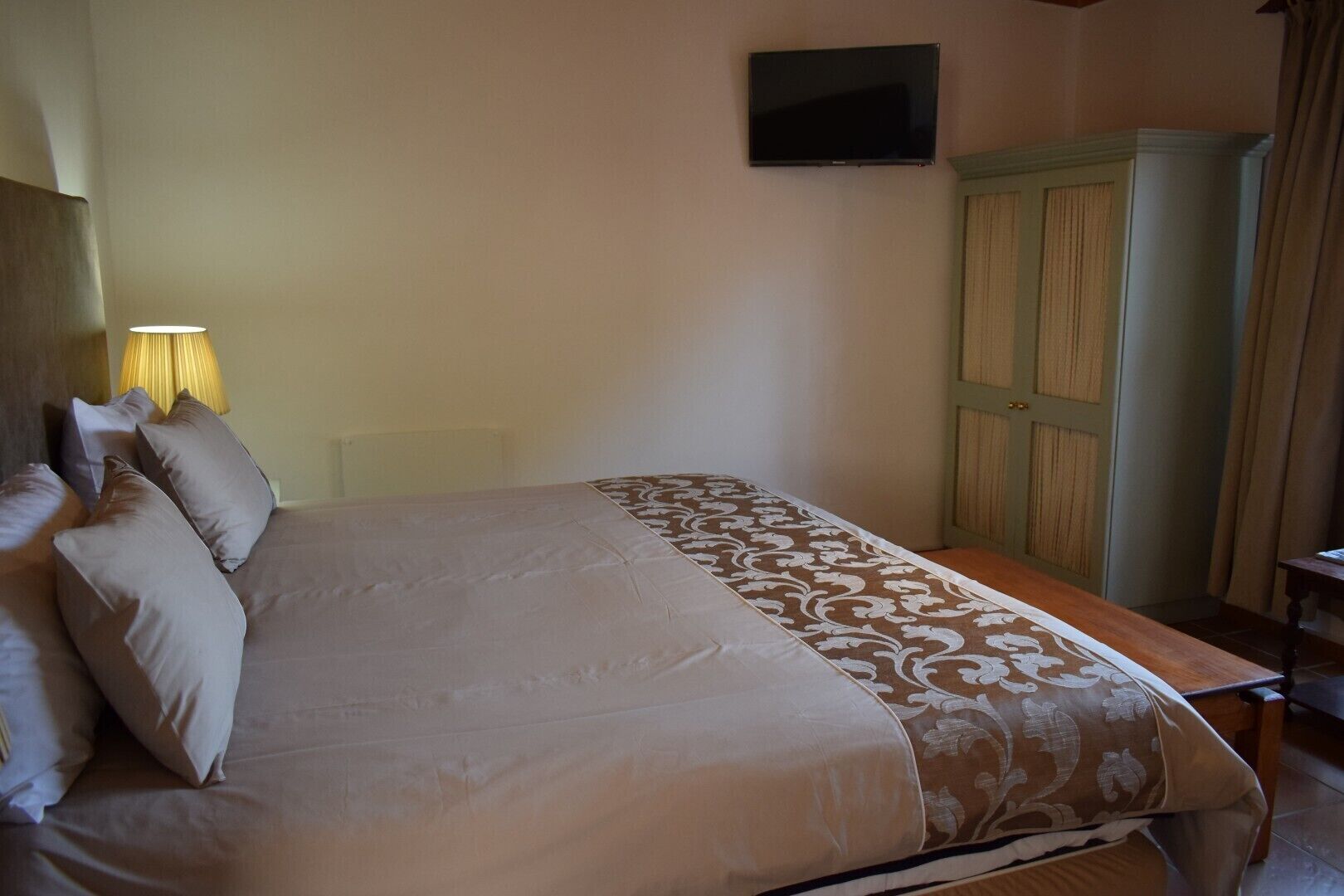 A neatly made bed with a patterned bedspread, a bedside lamp, and a wooden nightstand.