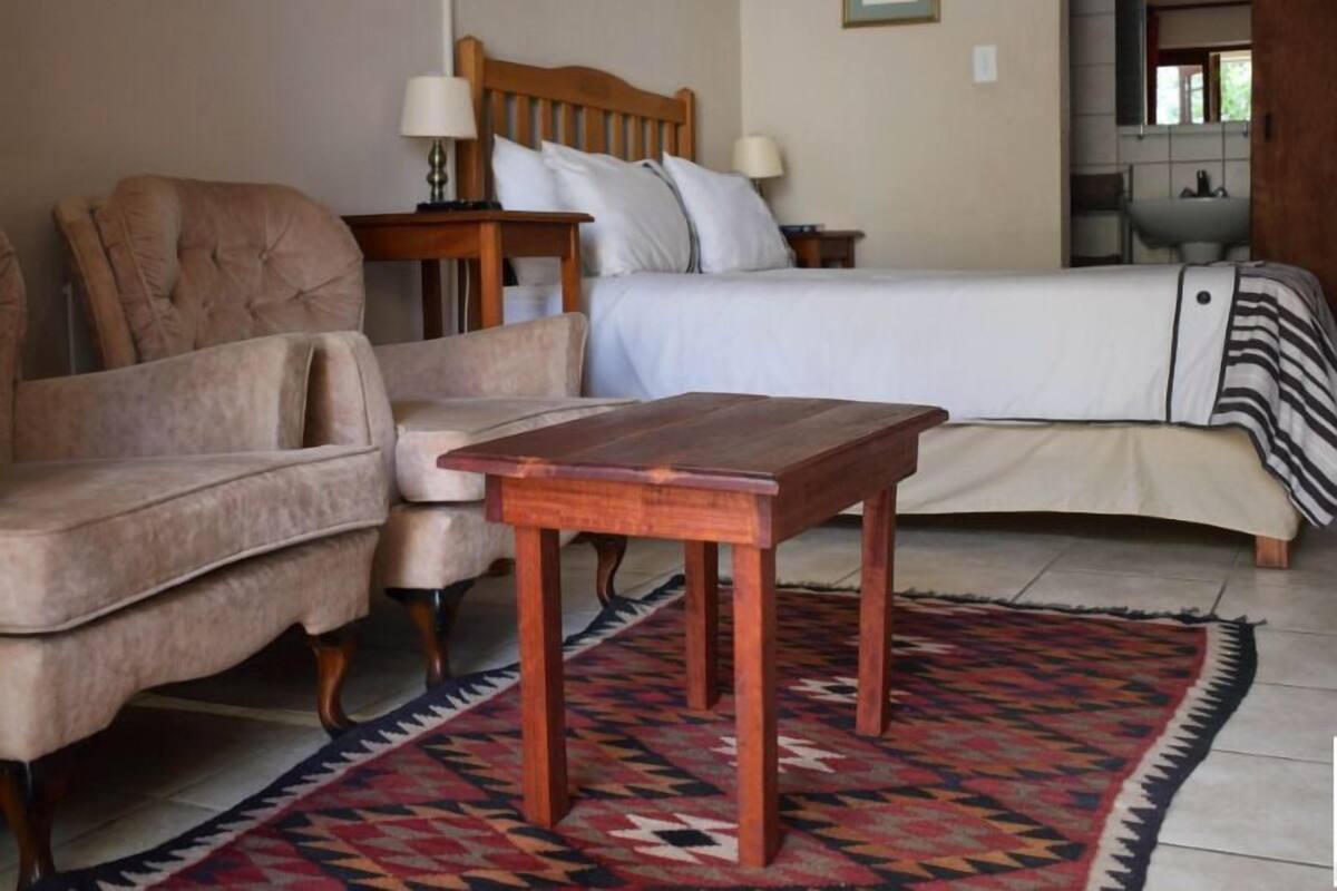 A bedroom with a bed, a wooden nightstand, a chair, a table, and a patterned rug.