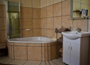 A bathroom with a corner bathtub, a sink, and a mirror. - Paul Kruger 63 (Robertson)