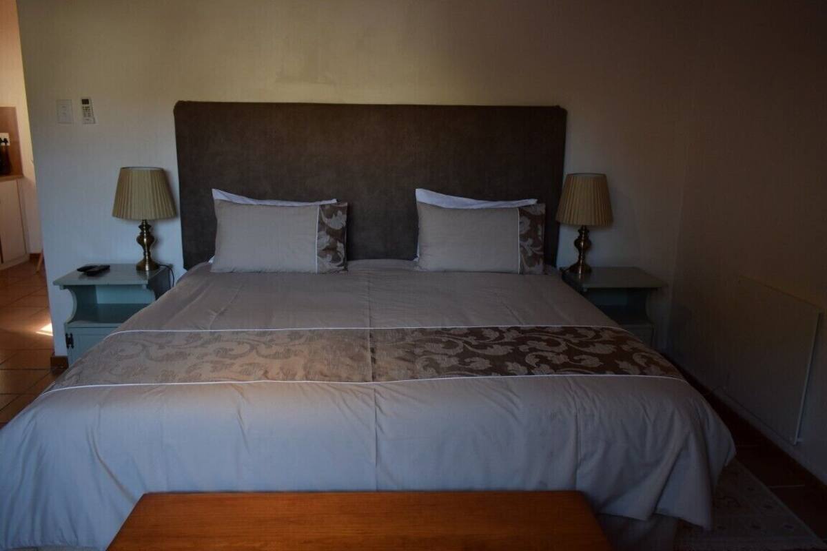 A neatly made bed with a headboard, two bedside tables with lamps, and a wooden bench in front of the bed.