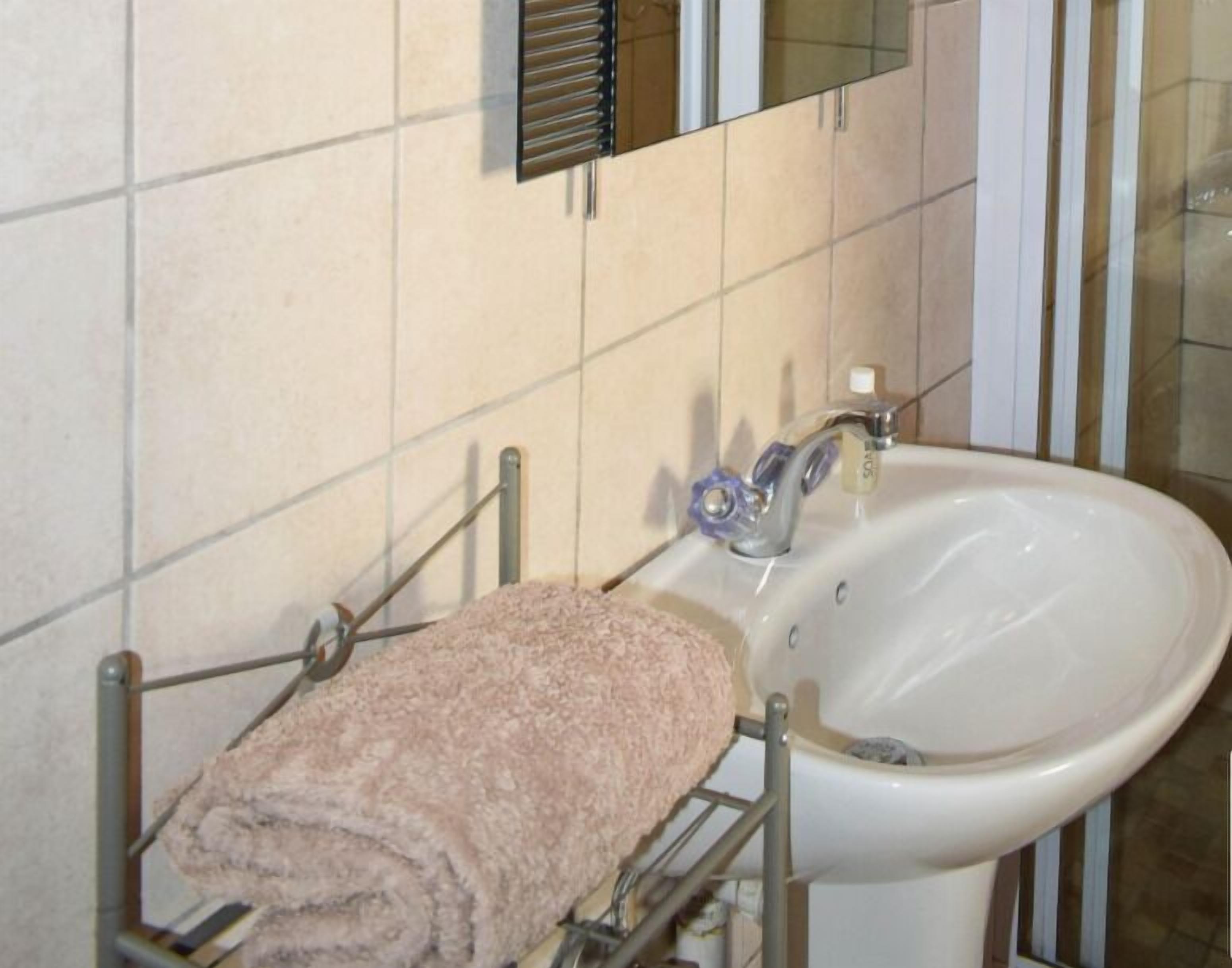 A bathroom with a white sink, a towel rack with a rolled towel, and a mirror above the sink.