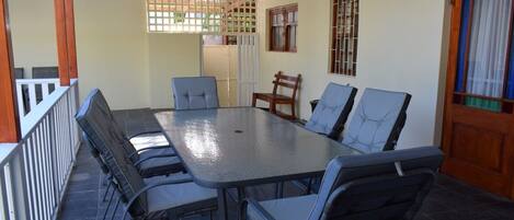 Un espacio de comedor al aire libre con techo, una mesa y sillas, una puerta de madera y una ventana con barrotes.