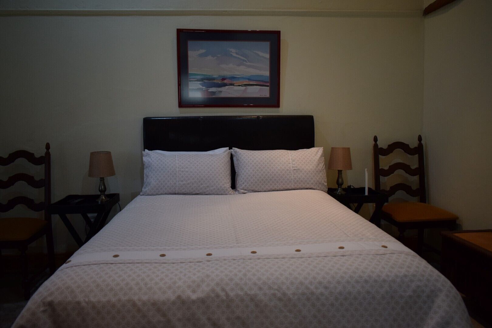 A neatly made bed with a patterned bedspread, two bedside tables with lamps, and a framed picture on the wall.