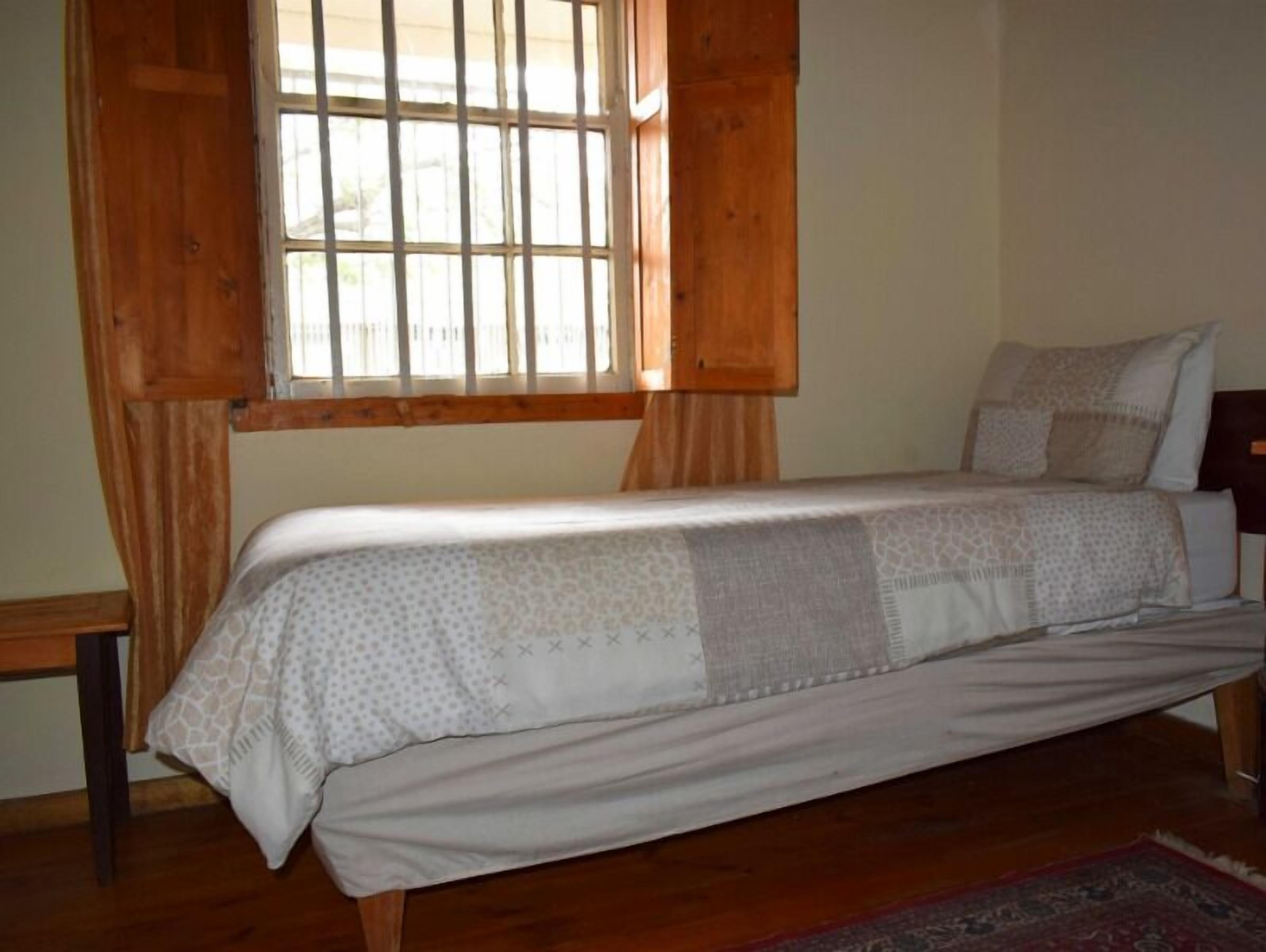 A single bed with a patterned bedspread, a wooden headboard, and a window with wooden shutters.