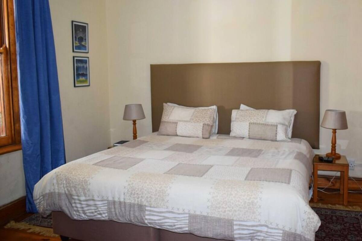 A neatly made bed with a patterned bedspread, two bedside lamps, and a framed picture on the wall.