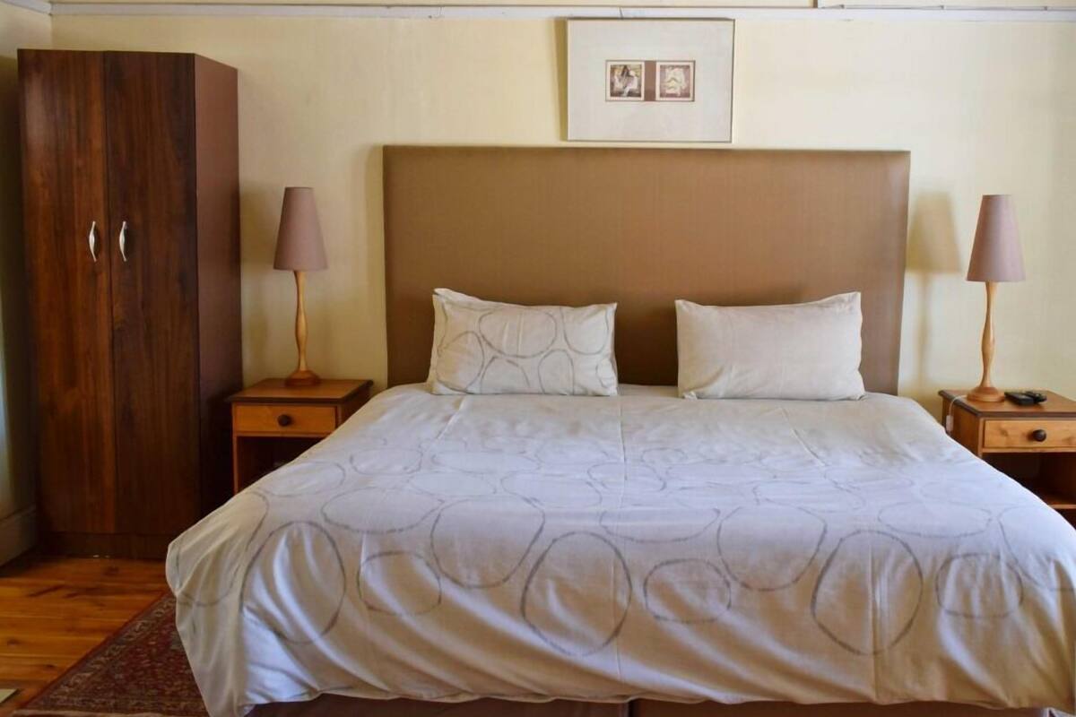 A bedroom with a large bed, two bedside tables with lamps, a wooden wardrobe, and a framed picture on the wall.