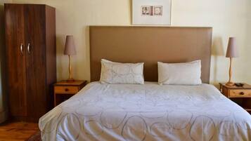 A bedroom with a large bed, two bedside tables with lamps, a wooden wardrobe, and a framed picture on the wall.