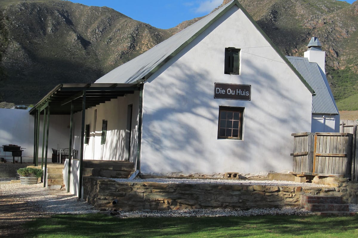 Un edificio blanco con un letrero que dice “Die Ou Huis” y un cimiento de piedra.
