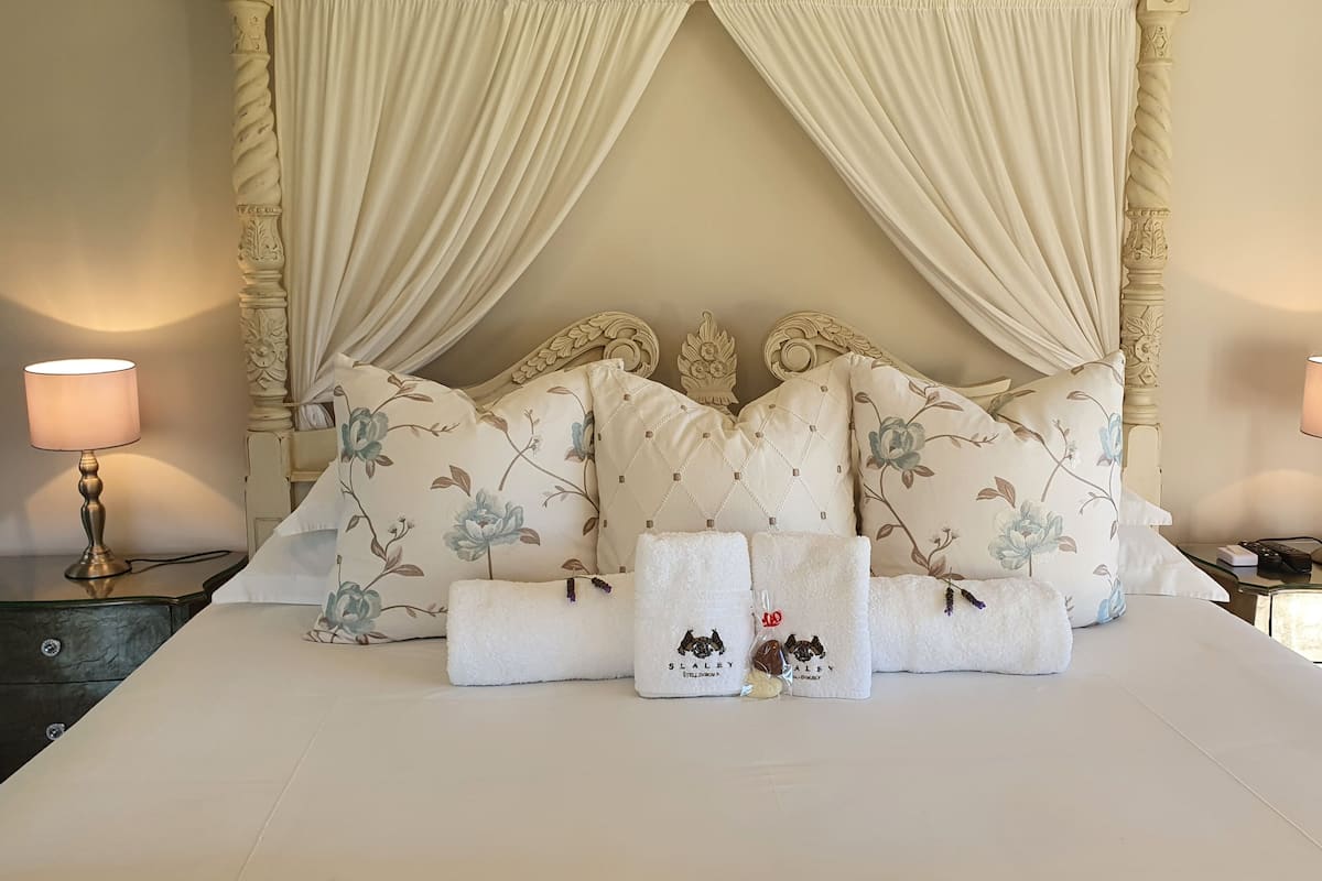 A neatly made bed with floral pillows, two bedside lamps, and a set of towels with a logo.