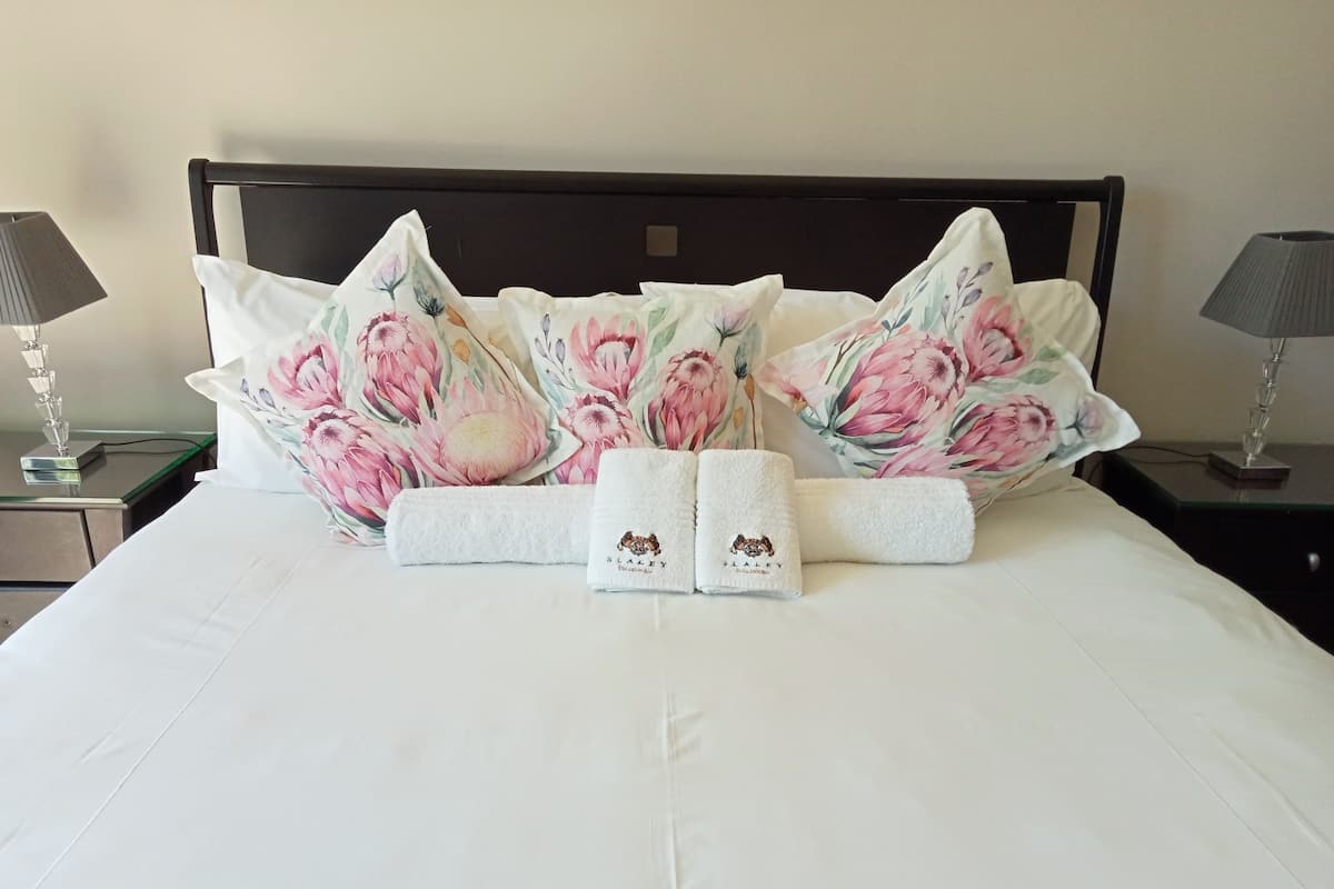 A neatly made bed with floral pillows and two towels with a dog logo.
