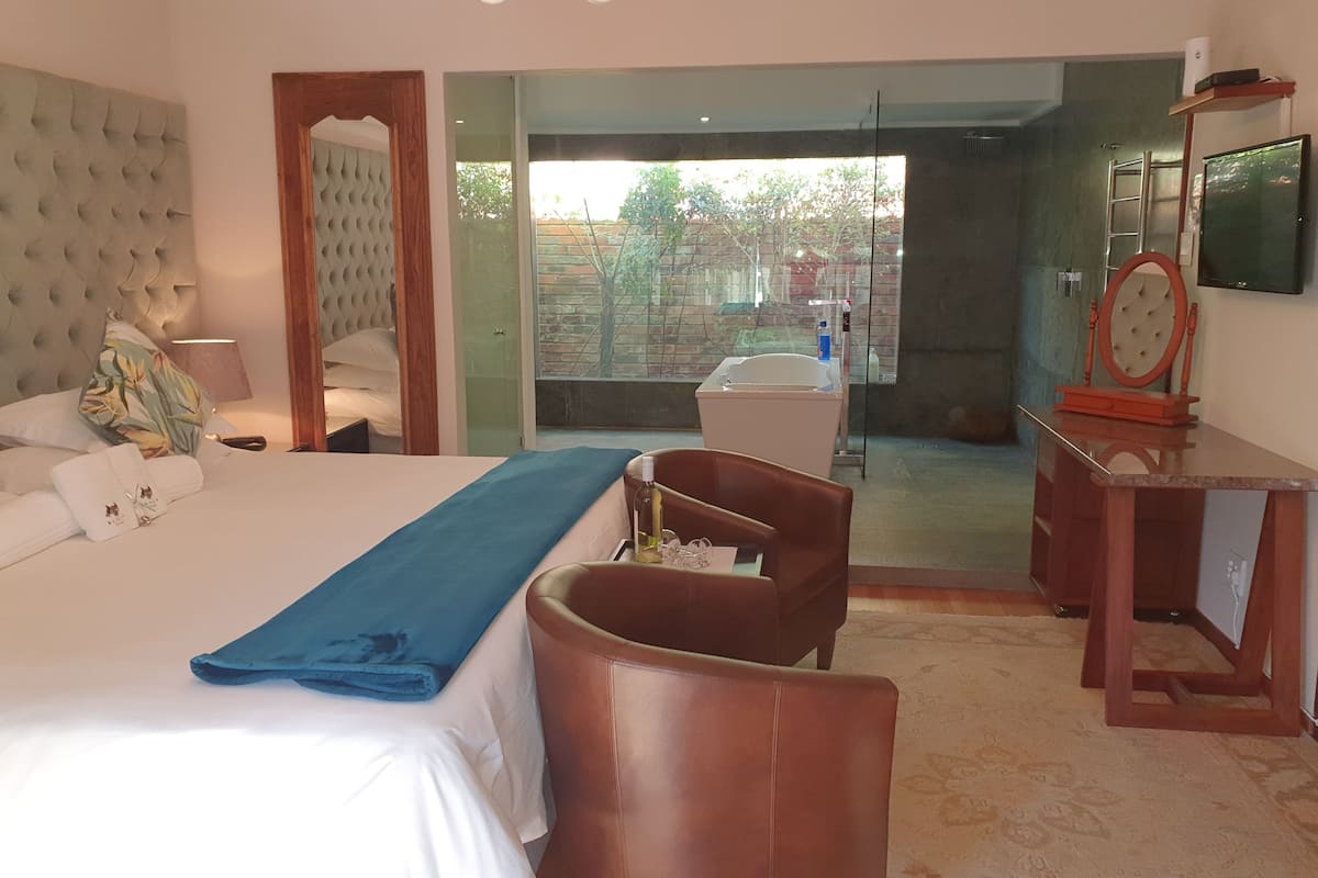 A hotel room with a large bed, a desk, a chair, a television, and a bathroom with a shower and toilet.