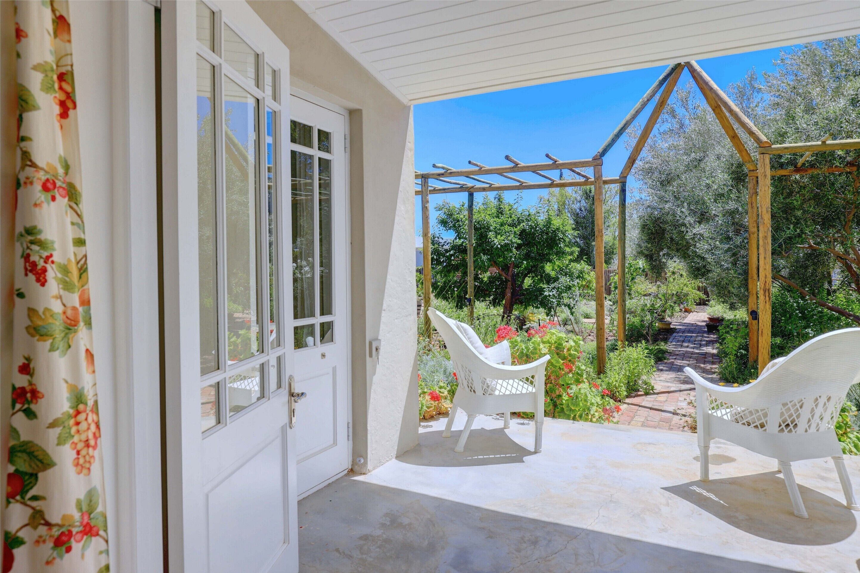 A covered patio with a white chair, a wooden pergola, and a garden path.