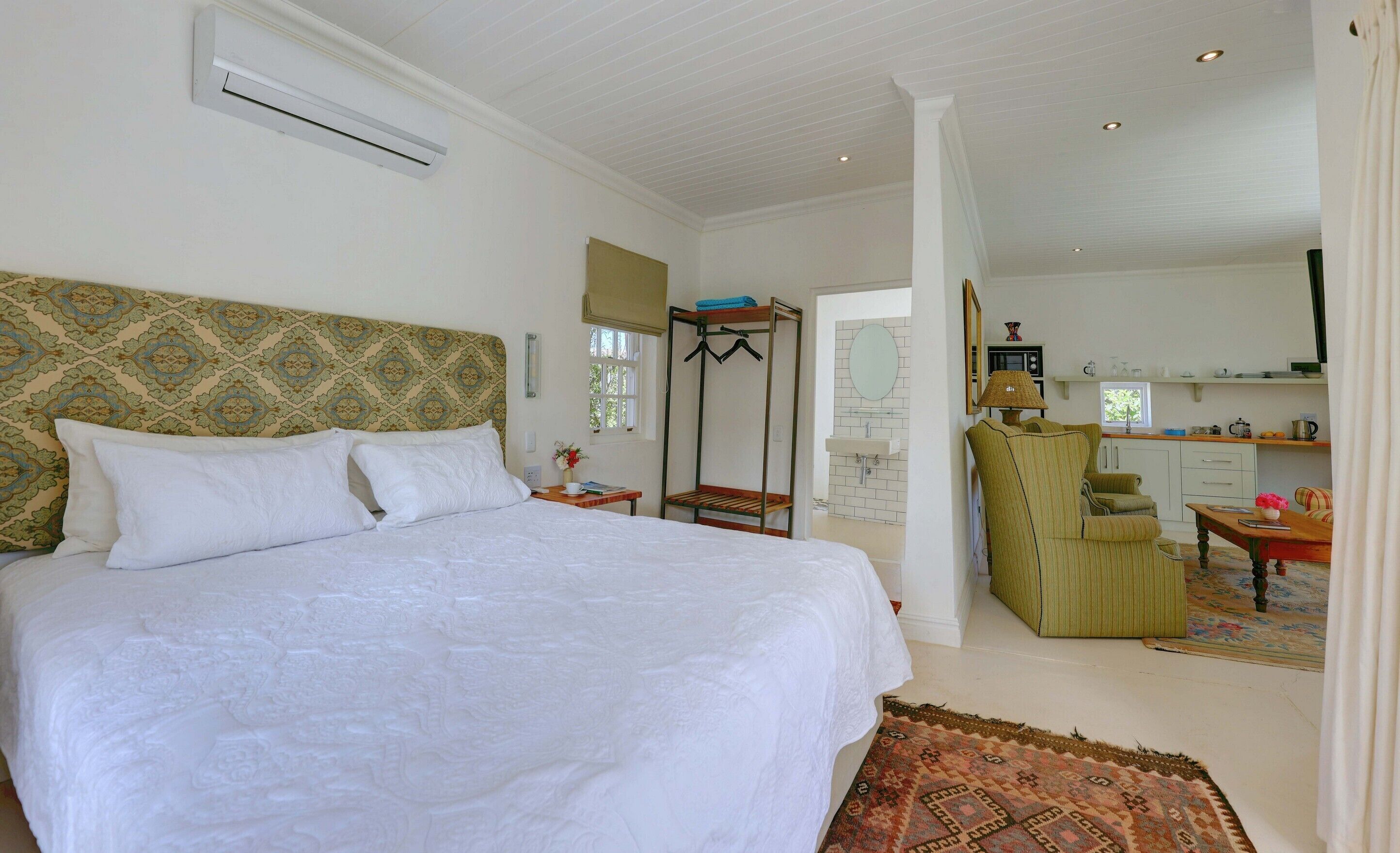 A bedroom with a large bed, a wardrobe, a desk, and a kitchenette.