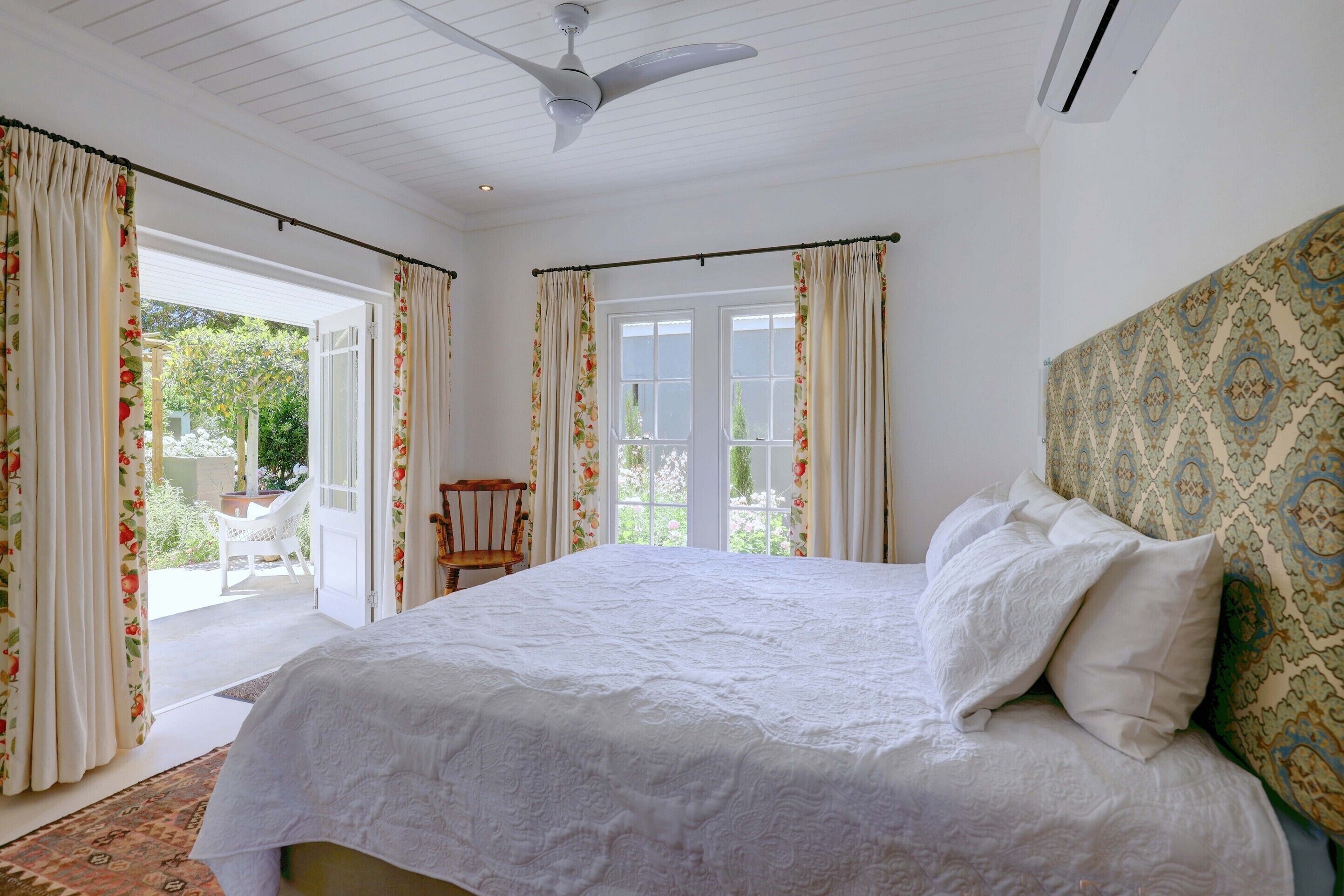 A bedroom with a large bed, a ceiling fan, and a view of the outdoors through a sliding glass door.
