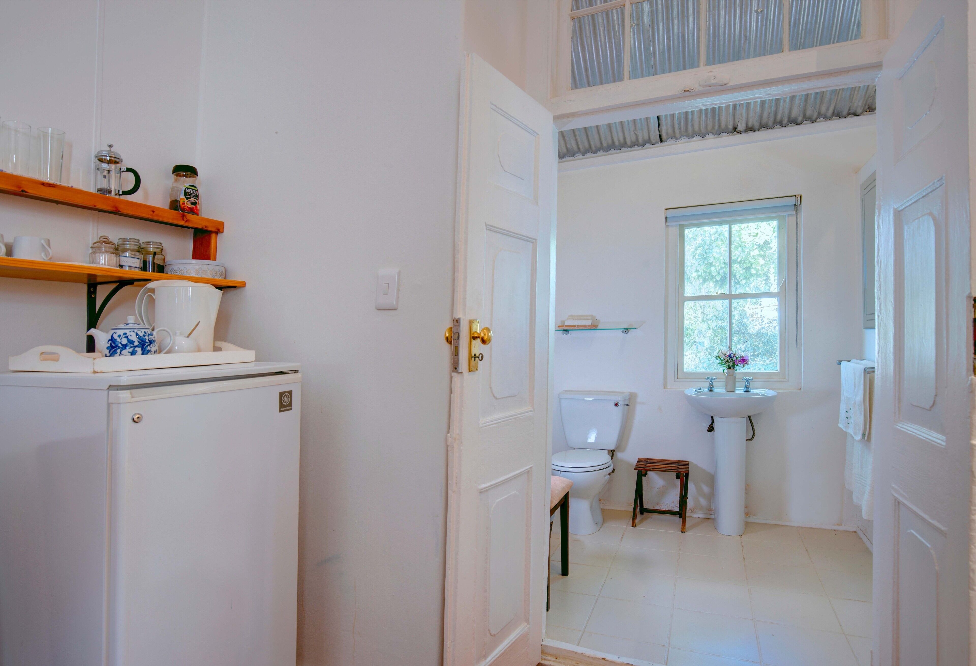 A compact bathroom with a toilet, sink, and shelves with toiletries.