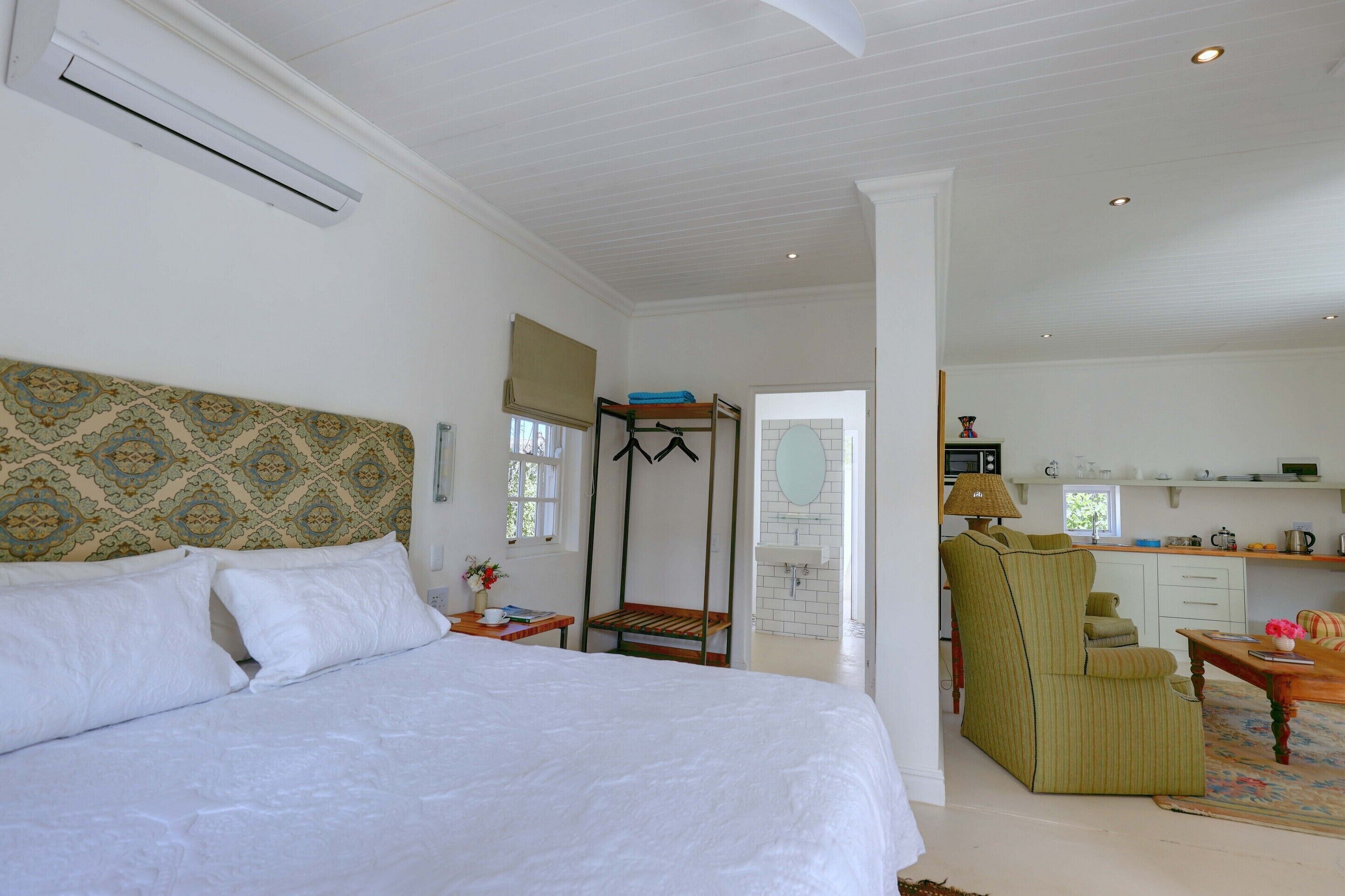 A bedroom with a bed, a wooden bench, a chair, a small table, and a window.