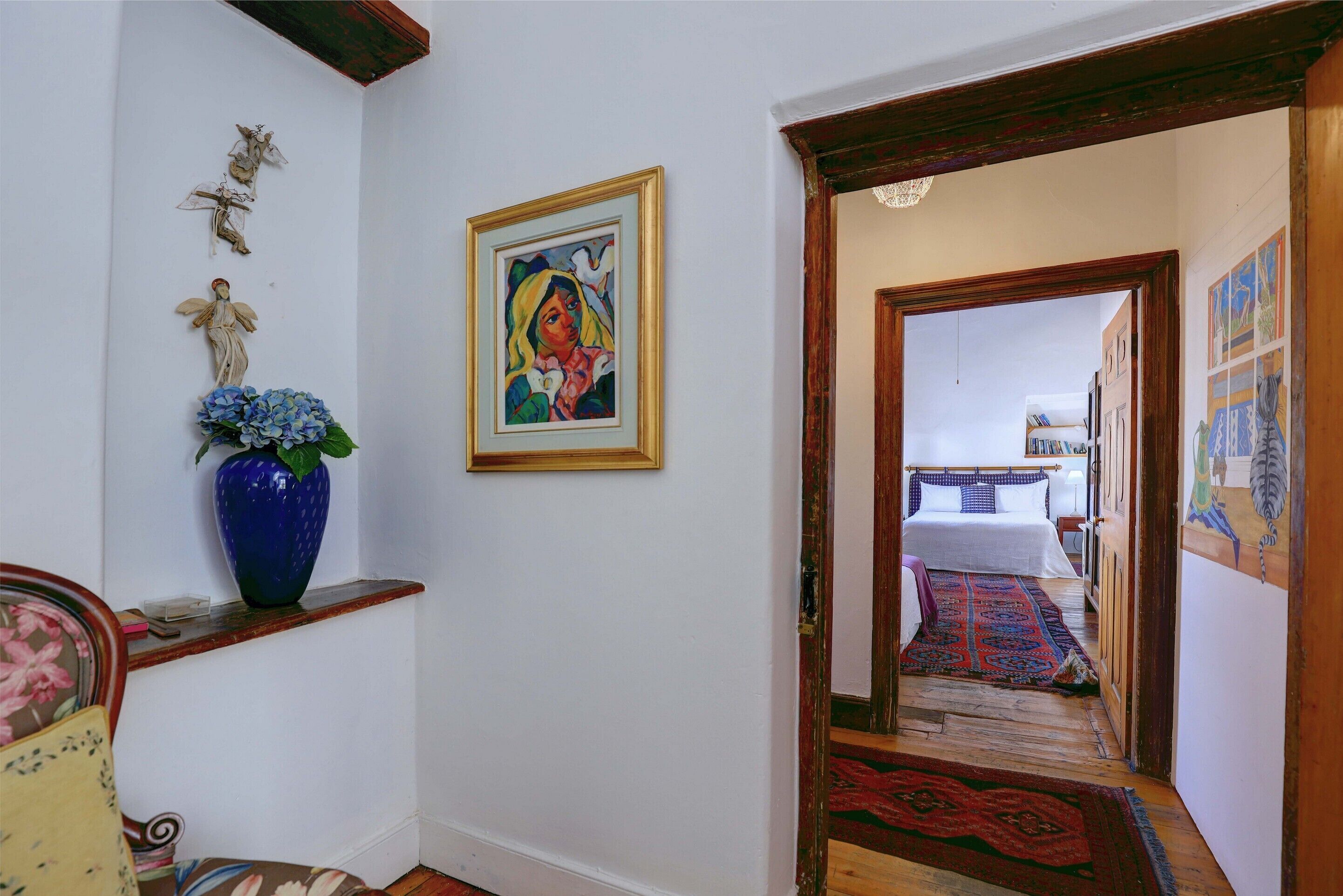 A hallway with a bed, a blue vase, and a framed painting.