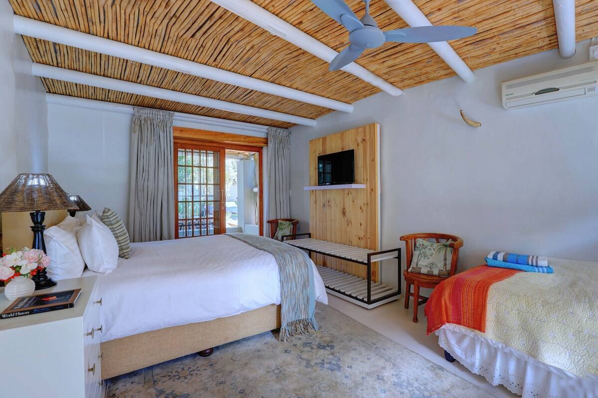 A bedroom with a bed, a desk, a chair, a ceiling fan, and a TV mounted on the wall.