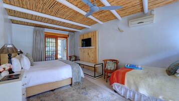 A bedroom with a bed, a desk, a chair, a ceiling fan, and a TV mounted on the wall.