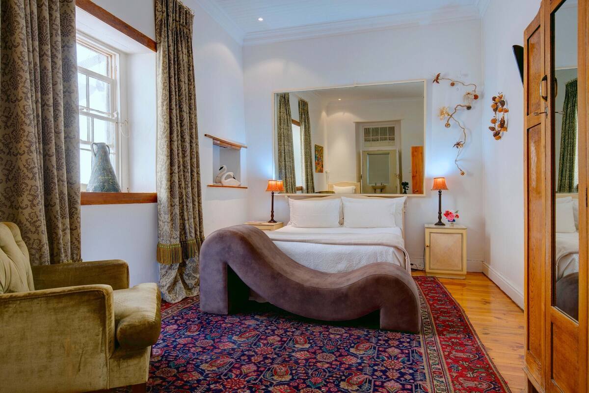 A bedroom with a large bed, a chair, a patterned rug, and a wooden floor.