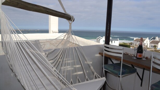 A hammock chair, a bar area with two stools, and a view of the ocean.