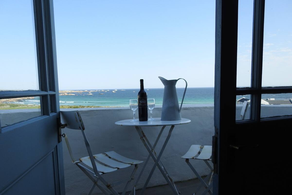 A balcony with a table, two chairs, a wine bottle, and a pitcher.