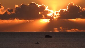 A sunset over the ocean with clouds and a silhouette of a boat.