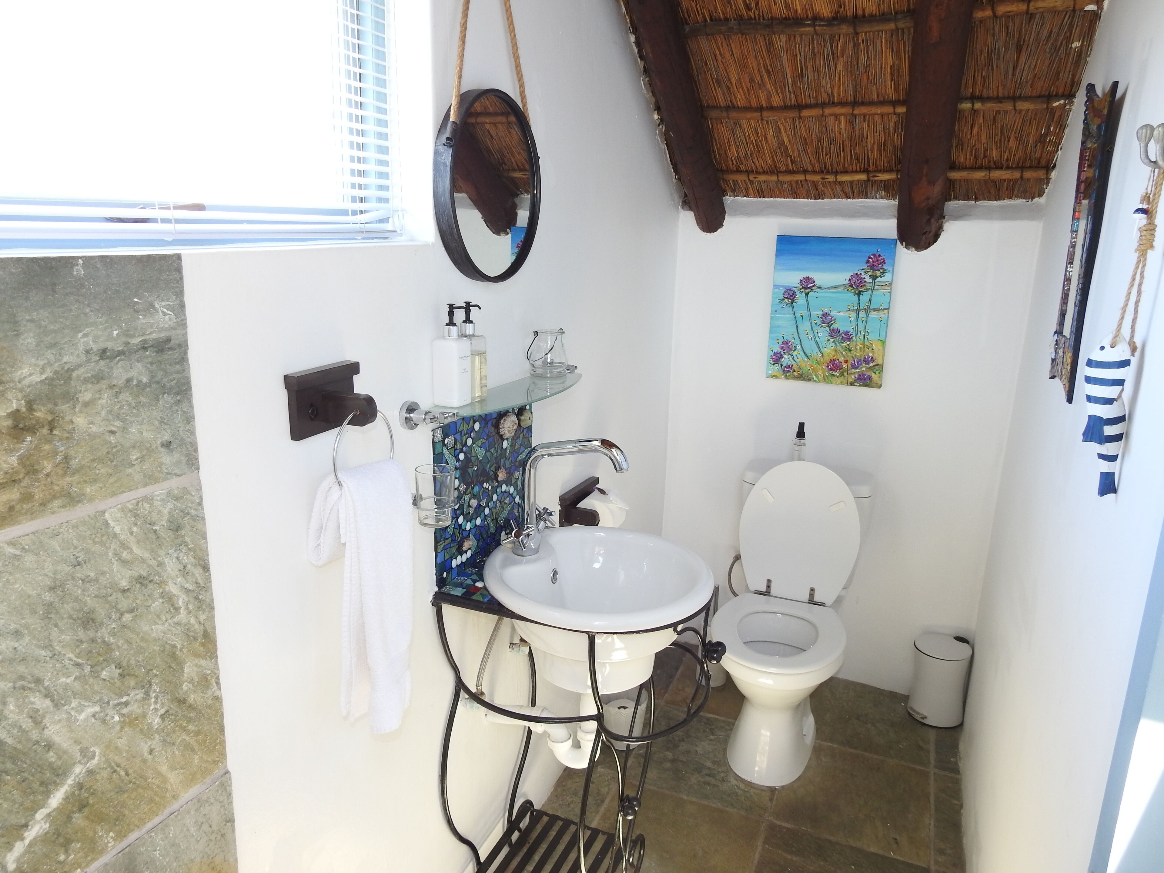 A bathroom with a white sink, a toilet, and a glass shelf with toiletries.