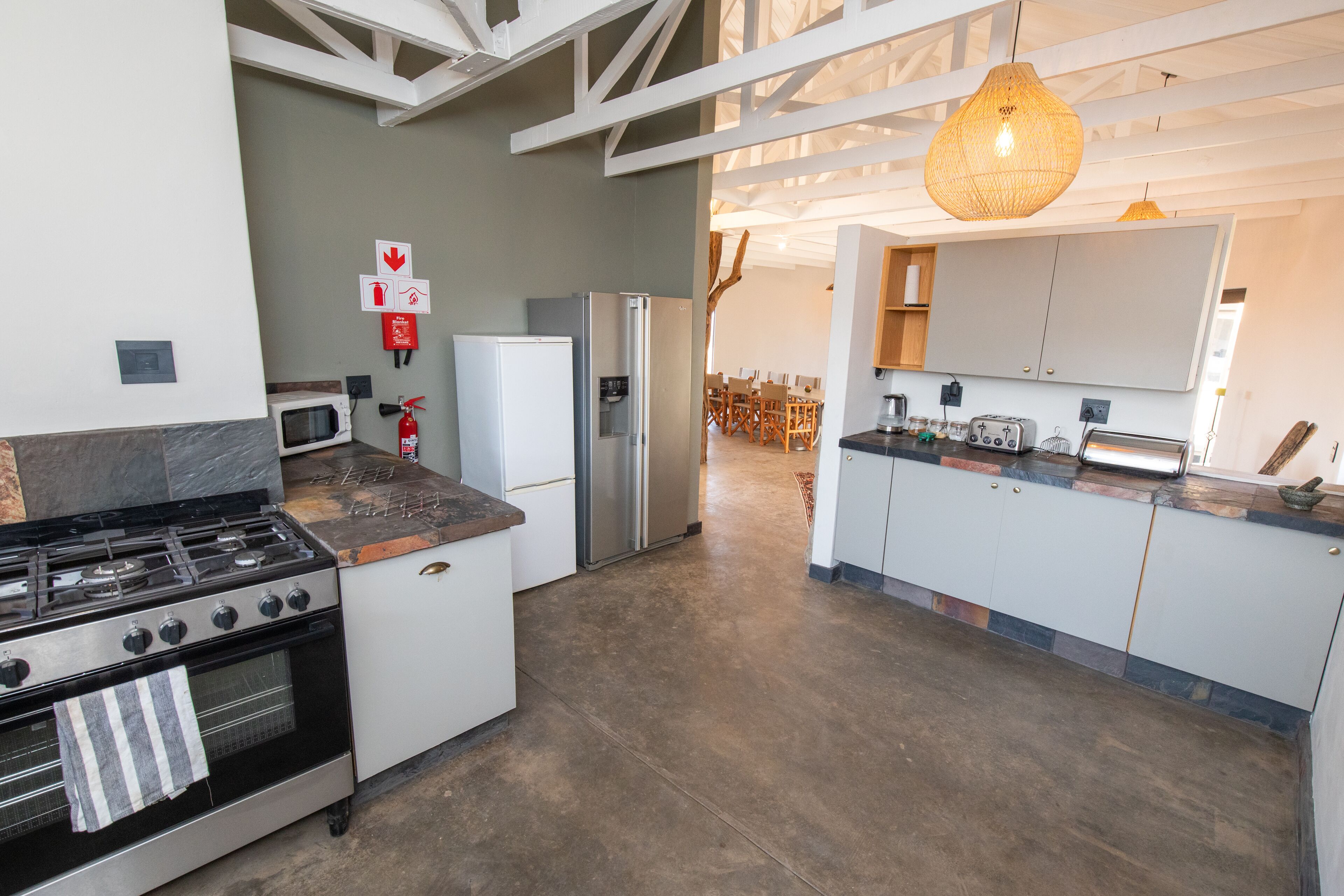 A modern kitchen with a gas stove, microwave, refrigerator, and a dining area with wooden chairs.