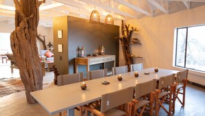 Uma sala de jantar moderna com uma mesa comprida, cadeiras de madeira e luminárias pendentes.
