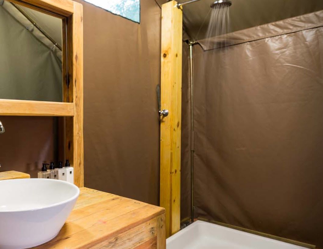 A bathroom with a wooden vanity, a white sink, a shower enclosure, and a mirror.
