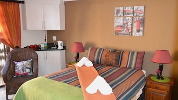 Et hotelværelse med en seng, to sengeborde, en stol, et lille tekøkken og en væg med et bybillede.