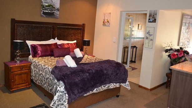 A bedroom with a large bed, a nightstand, a dresser, and a door leading to a bathroom. - Ikhanda Guesthouse (Mashishing)