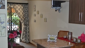 A kitchen with a marble countertop, wooden cabinets, and a dining area with wicker chairs. - Ikhanda Guesthouse (Mashishing)