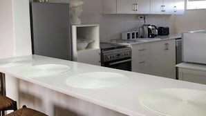 A modern kitchen with white countertops, a central island with seating, and pendant lighting. - Stell On Air (Stellenbosch)