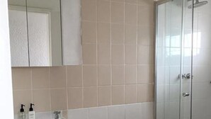 A bathroom with a shower, a sink with toiletries, and a mirror. - Stell On Air (Stellenbosch)