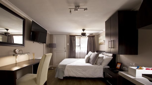 A bedroom with a bed, a desk, a chair, a television, and a ceiling fan. - Faith, Hope & Love (Gqeberha (Port Elizabeth))