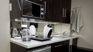 A modern kitchen with dark wood cabinets, a built-in microwave, a kettle, a coffee maker, and a dishwasher. - Faith, Hope & Love (Gqeberha (Port Elizabeth))