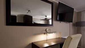 A hotel room with a large mirror, a flat-screen TV, a desk with a lamp, and a chair. - Faith, Hope & Love (Gqeberha (Port Elizabeth))