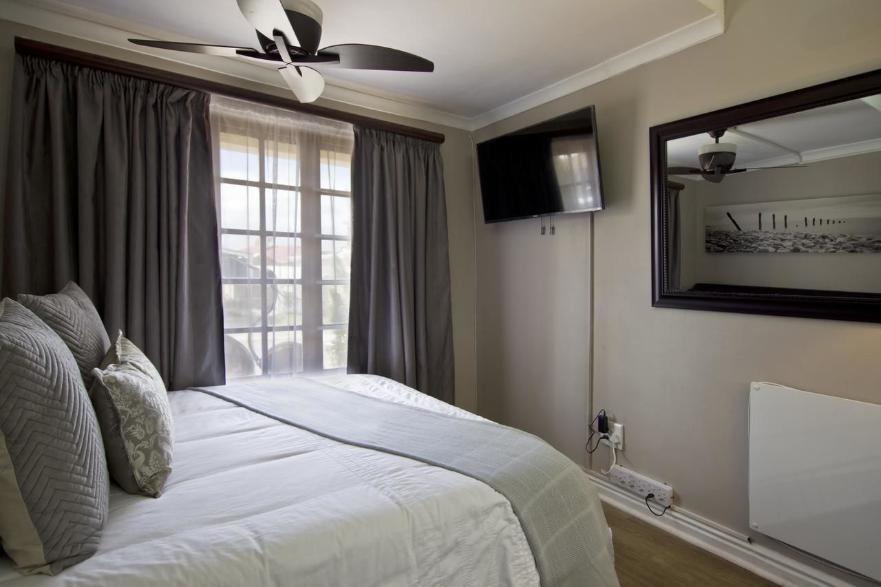 A bedroom with a bed, curtains, a ceiling fan, a TV, and a radiator.