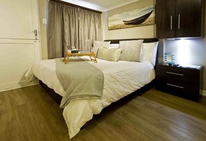 Una cama bien hecha con una bandeja de desayuno, una mesita de noche con una lámpara y un cuadro de un barco en la pared.