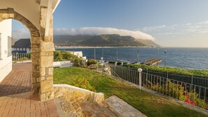 A coastal property with a stone archway, a paved pathway, and a view of the sea and a mountain with clouds. - Sunny Cove Manor (Cape Town)